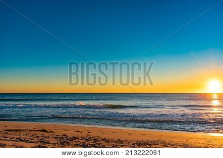glowing yellow sun rising on the horizon on a cool clear morning at the beach