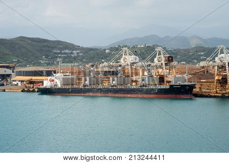 NOUMEA, NEW CALEDONIA, PACIFIC ISLANDS-NOVEMBER 25TH, 2016: Cargo ship moored at commercial dock with island landscape under an overcast sky in Noumea, New Caledonia