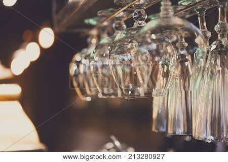 Glasses hanging on bar rack close up. Clean utensil for wine and cognac in restaurant, barroom background