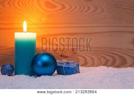 Avent candle and christmas decoration isolated on wood background. Christmas background with snow, candle and blue gift box.