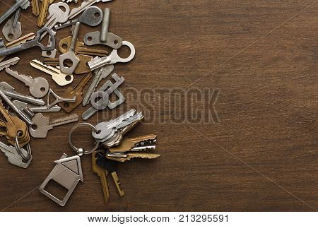 Bunch of keys with house shaped trinklet against wooden background and collection of different keys. Safety, security and real estate concept, top view, copy space