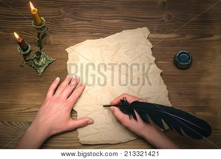 Man signing agreement or contract with feather pen in his hand on blank crumpled paper page with copy space. Person writes a letter. Writer desk table.