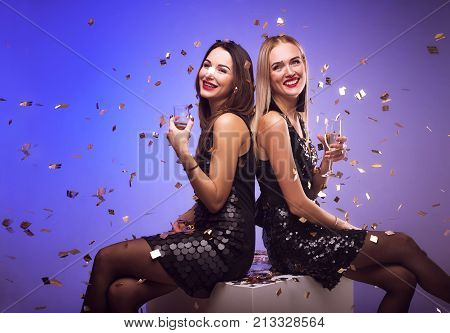 Young attractive women celebrating a party drinking champagne and dancing while confetti falling