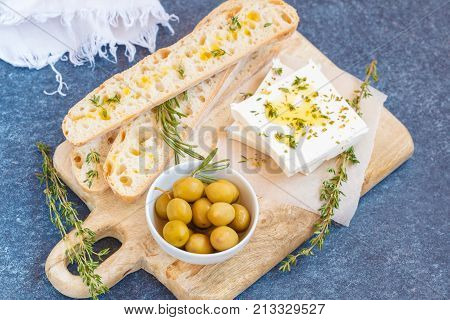 Green olives feta cheese and fresh ciabata on a wooden board dark background top view.