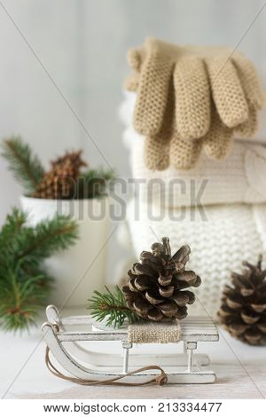 Winter concept with white blanket pullover, gloves, sleds, cup, cones and fir branches. Selective focus.