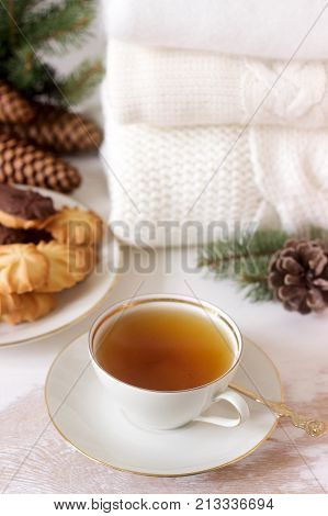 Winter composition with tea and biscuits in the background of a rug or pullover, cones and fir branches. Selective style.