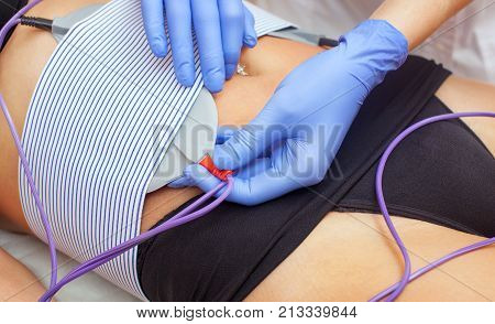 The procedure of myostimulation oon the belly and hips of a woman in a beauty salon. Caring for the body reducing excess weight.