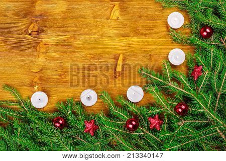 Top view of green fresh fir branches with red Christmas decorations and a burning candle frame on an old wooden background with copyspace. Christmas New Year