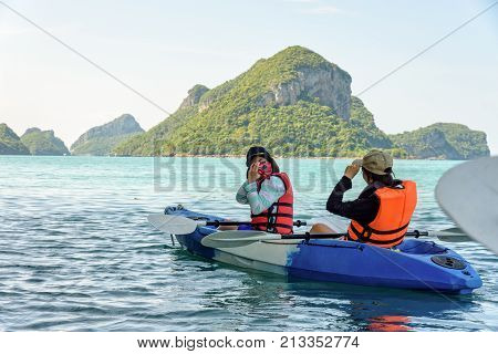 Two women are mother and daughter using a camera take pictures on kayak while travel by boat with happy on the sea during summer at Ko Wua Ta lap islands