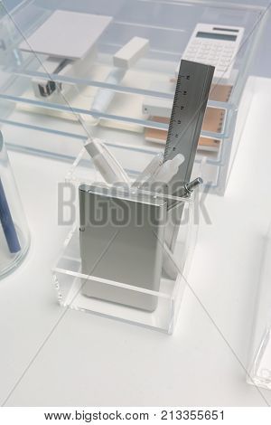 Square shape clear acrylic holder for stationery organizer on white office table against blurred background.
