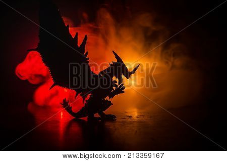 Silhouette Of Fire Breathing Dragon With Big Wings On A Dark Orange Background. Empty Space