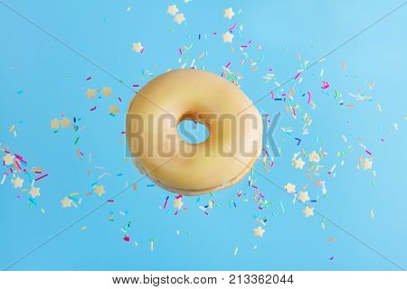 one flying sweet doughnut in glaze with sprincles on blue
