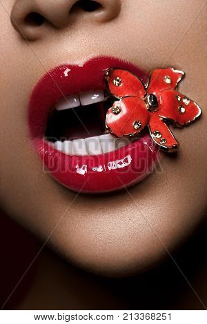 closeup shot of full sexy woman lips with red lipstick. metal jewerely flower in mouth. copyspace.