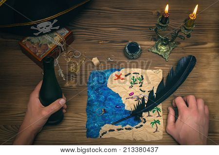 Crumpled treasure map and pirate hat on wooden table. Treasure hunt. Pirate man drinks rum from bottle and learning treasure map where buried gold chest marked on the map.