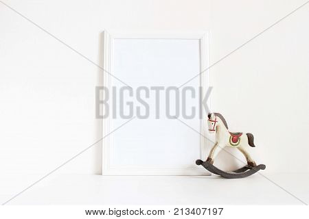 White blank wooden frame mockup with old wooden horse toy on the white table. Styled stock feminine photography. Home decor, Christmas winter concept.