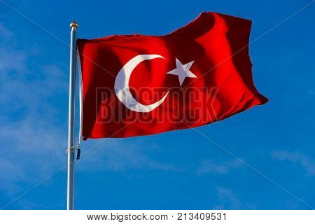 Flag of Turkey on flagpole waving in the wind against the blue sky close up