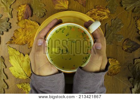 cup of hot soup warming hands autumn in yellow leaves