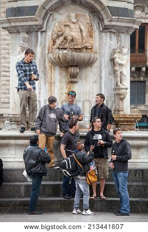 CATANIA, ITALY. April 3, 2015: A group of American tourists is under a monument in the center of Catania in Sicily, Italy. Near them some street vendor.