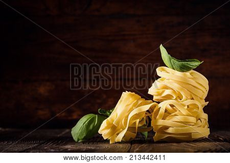 Background of few piles of pasta composed with fresh green basil leaves on wood.