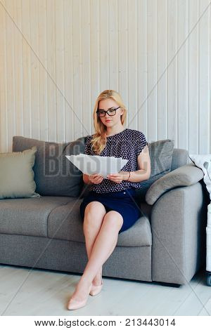 beautiful blond woman with glasses sits on the couch and throws up paper 1