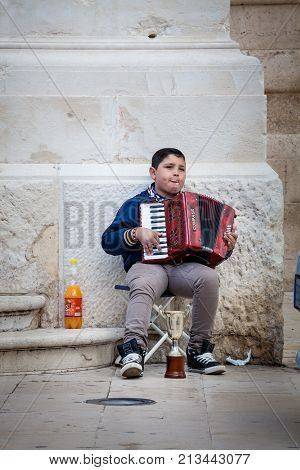 SYRACUSE, ITALY. April 3, 2015: Accordion player, poor child busker in the street in the center of Syracuse in Italy, Sicily. He asks offers to passersby.
