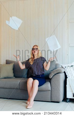 beautiful blond woman with glasses sits on the couch and throws up paper 1