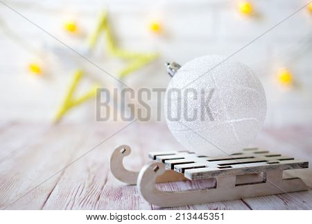 Shining Christmas Ball On Toy Wooden Sled On Light Bokeh Background With Goolden Star. New Year Card