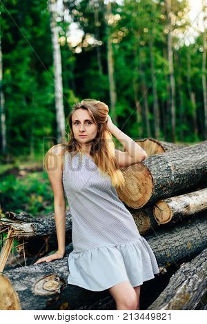 Girl in a blue dress near a fallen tree on a background of a forest in summer weather, a wooden spittle of a tree 1