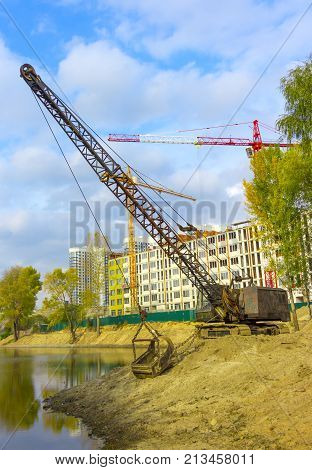 Excavator standing on the shore clears the bottom of the lake from dirt and debris