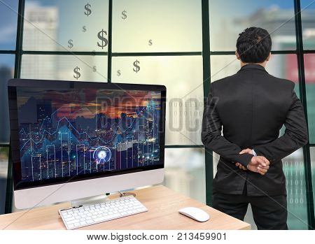 the computer on the wood table with trading graph at the screen in front of the glass window over on the trading graph over the blurred photo of cityscapeBack side of Businessman