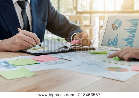 young business man hoding pen point notebook with partner using tablet graph chart and post it note for Plans to improve quality next month.