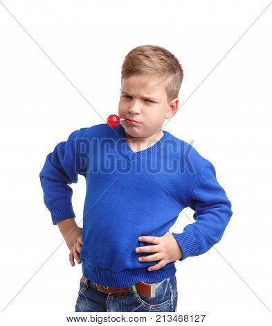 A boy in a blue sweater with a stick with a lollipop in his mouth is standing arms in the sides. With a menacing and serious look on a white isolated background