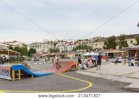 Teens Summer Evening Ride Skateboards And Bicycles On City Streets. The Area Of The Tercentenary Of