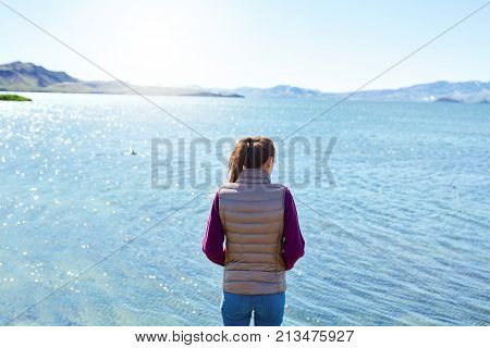 back view of woman on the shore of tne Thingvallavatn lake in Thingvellir National Park, largest natural lake in Iceland. Travel to Iceland.