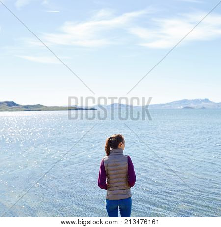 back view of woman on the shore of tne Thingvallavatn lake in Thingvellir National Park, largest natural lake in Iceland. Travel to Iceland.