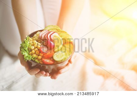 Girl in white jeans holds in hands fork, vegan breakfast meal in bowl with avocado, quinoa, cucumber, radish, salad, lemon, cherry tomatoes, chickpea, chia seeds. Top view, copy space. Clean eating.