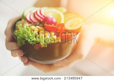 Girl in white jeans holds in hands fork, vegan breakfast meal in bowl with avocado, quinoa, cucumber, radish, salad, lemon, cherry tomatoes, chickpea, chia seeds. Top view, copy space. Clean eating.