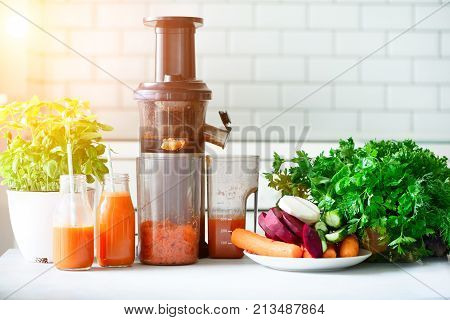 Woman making fresh drink. Juicer and carrot juice. Fruits in background. Clean eating, detox concept. Sunny morning with sunlight. Toned effect