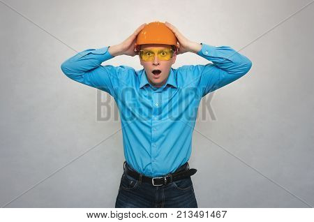 Confused builder worker with open mouth holding a head with his hands and in shocked from from what happened. Accident in production or construction. Stress situation.