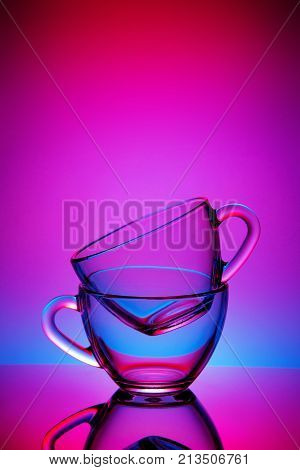 Two cups and saucers of glass. Tea is poured into the top Cup. Helium filter gives a beautiful light. Studio photos using the backlight. The reflection on the black table. The background is orange-red.