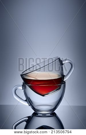 Two cups and saucers of glass. Tea is poured into the top Cup. Helium filter gives a beautiful light. Studio photos using the backlight. The reflection on the black table. The background is blue.