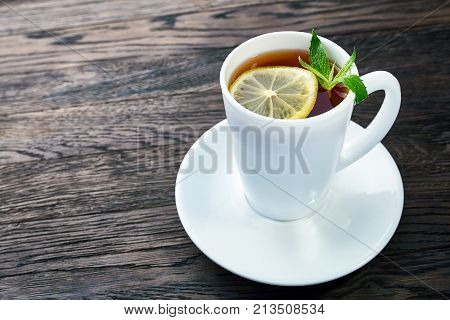 Tea with lemon in white cup, cinnamon sticks, knitted woolen scarf on a wooden table