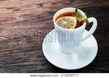 Tea with lemon in white cup, cinnamon sticks, knitted woolen scarf on a wooden table