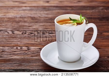 Tea with lemon in white cup, cinnamon sticks, knitted woolen scarf on a wooden table