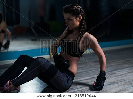 Young fighter boxer girl wearing boxing gloves sitting on the floow near mirror in gym.