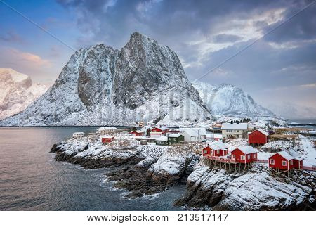 Famous tourist attraction Hamnoy fishing village on Lofoten Islands, Norway with red rorbu houses. With falling snow in winter on sunrise