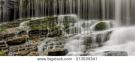 Wide format panorama of waterfall crashing over rocks and moss