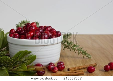 A full bowl of cranberries surrounded by seasonal greens and cinnamon sticks.