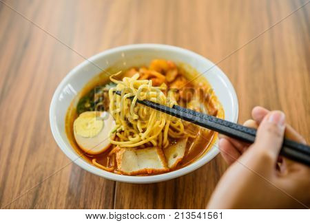 Hand with Chinese chopsticks eating noodle a famous Malaysia prawn noodle cerry soup.