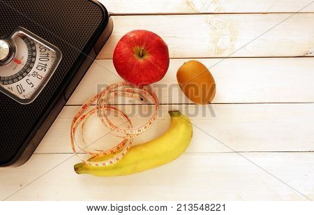 Black weight scale ,fresh fruit and measure tap on white wooden floor Fitness concept,diet and exercise  for losing weigh